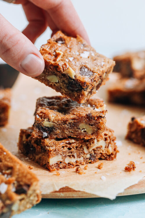 Picking up a vegan gluten-free chocolate chip cookie bar from a stack